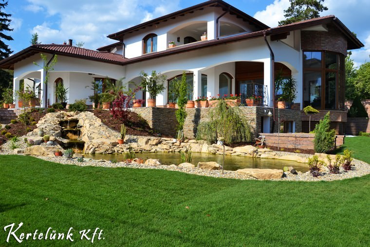 Zöld gyepszőnyeggel kerített kerti tó és sziklakert.